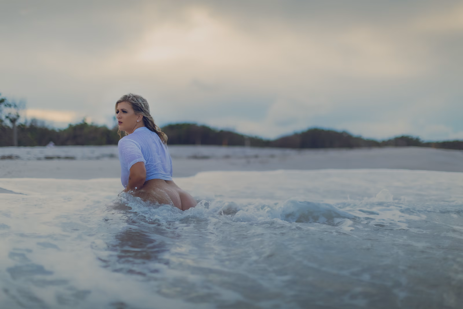 Woman in a wet white shirt kneeling in shallow ocean water
